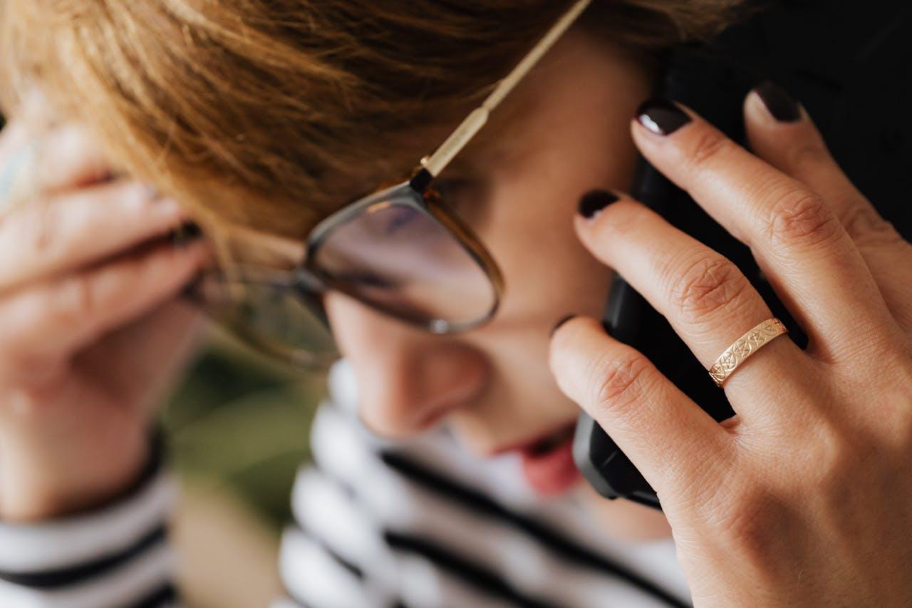 A person holding their glasses while taking a phone call